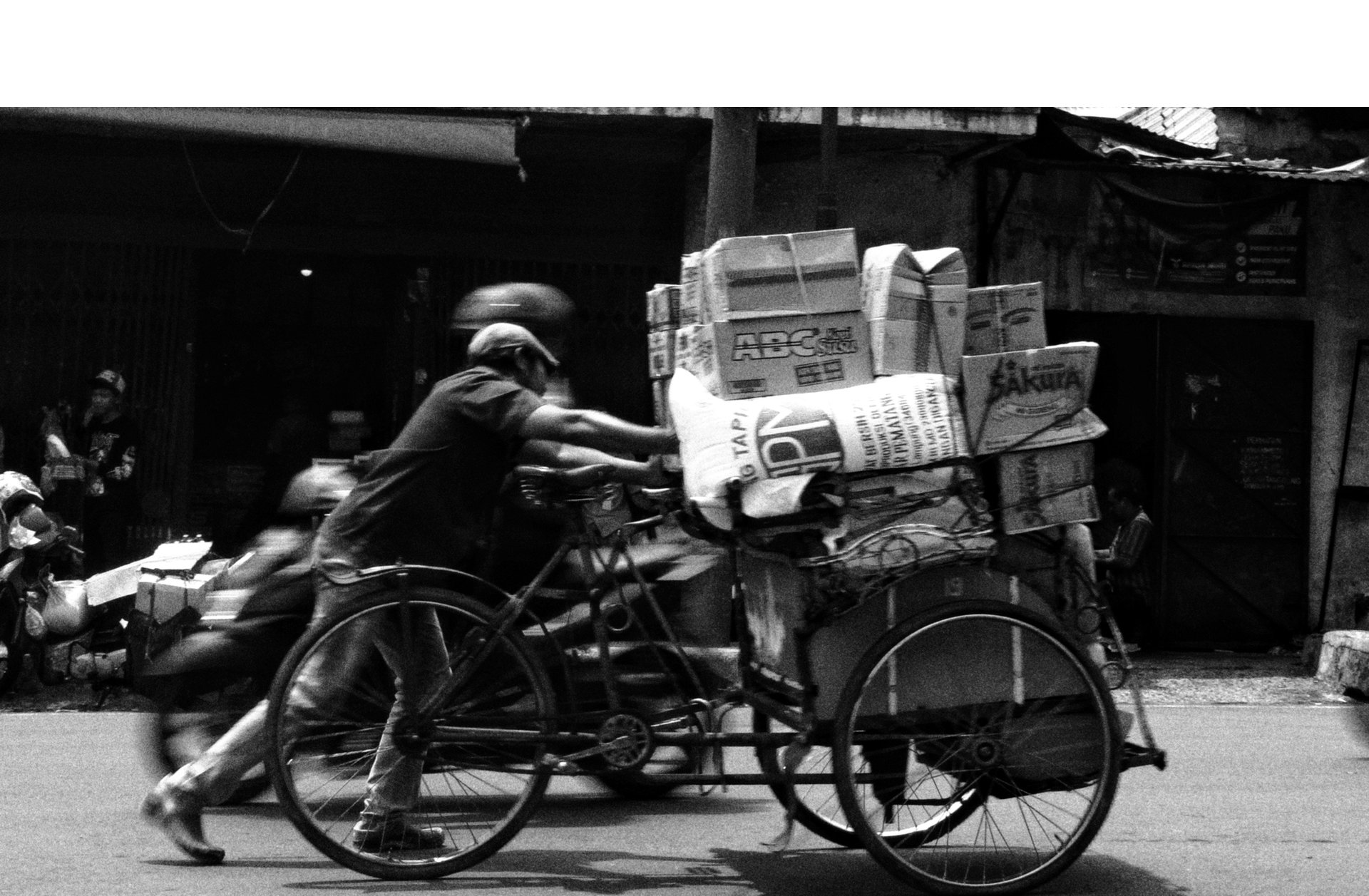 Man in Indonesia pushing a delivery tricycle loaded with packages.